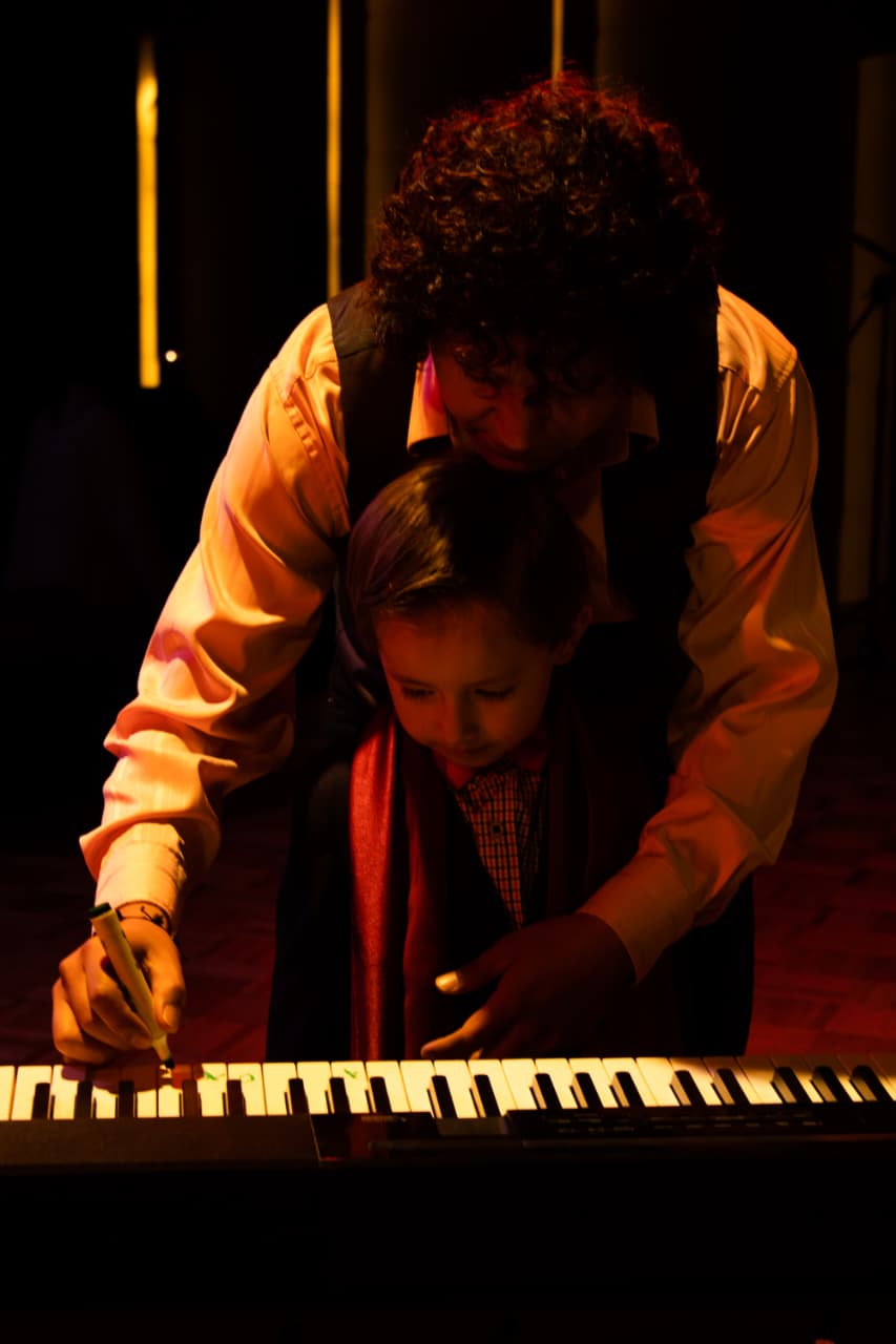 Docente acompañando a un niño frente al piano en un concierto