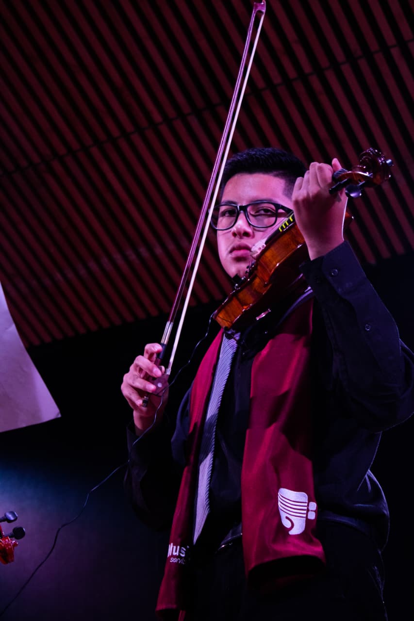 Músico interpretando violín bajo las luces del escenario